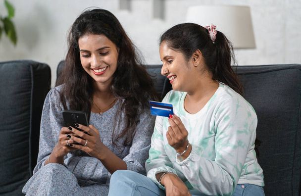 Heureuses jeunes sœurs indiennes effectuant un paiement en ligne à l'aide d'une carte de crédit sur téléphone mobile concept d'amitié, de banque ou de shopping financier et de commerce électronique - Photo, image