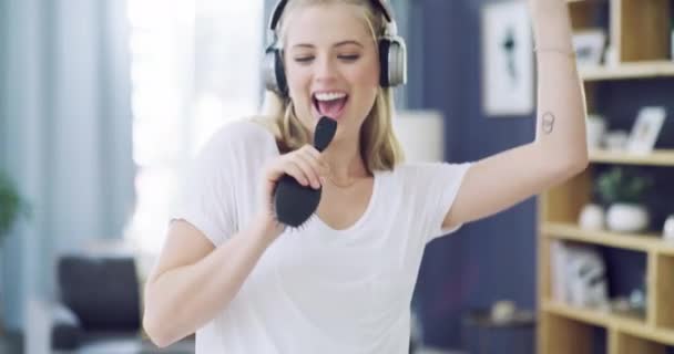 woman, dancing and singing with brush or headphones sound, music streaming or listening. Female person, comb and radio audio moving or playlist song in living room, apartment happy for connection. - Footage, Video