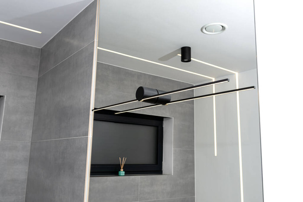 LED light strips mounted in the wall and ceiling in a modern bathroom, visible black wall lamp. - Photo, Image