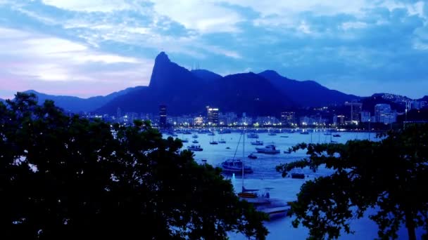 Zeitraffer aus der Perspektive der Botafogo-Bucht in Rio de Janeiro, Brasilien bei Sonnenuntergang mit der Christus-Erlöser-Statue - UNESCO-Weltkulturerbe - Filmmaterial, Video