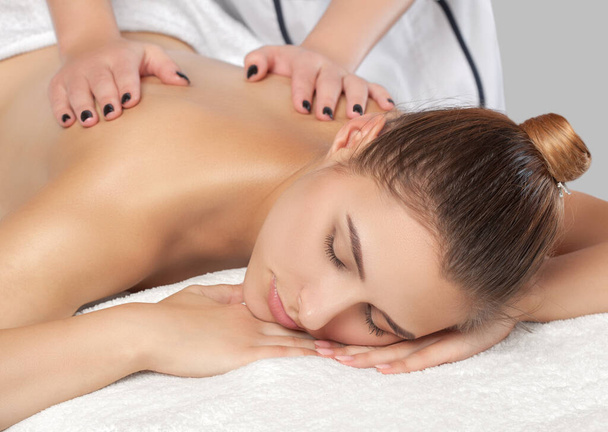 Masér provádí relaxační masáž krku, ramen a zad mladé krásné ženy v lázních. Koncepce kosmetiky a masáží. - Fotografie, Obrázek