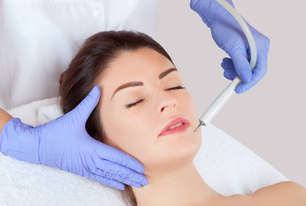 The cosmetologist makes the procedure treatment of Couperose and face cleaning of the skin of a beautiful, young woman in a beauty salon.Cosmetology and professional skin care. - Photo, Image
