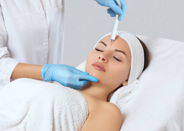 Kosmetolog wykonuje zabieg oczyszczania skóry pięknej, młodej kobiety w salonie kosmetycznym.Kosmetologia i profesjonalna pielęgnacja skóry. - Zdjęcie, obraz
