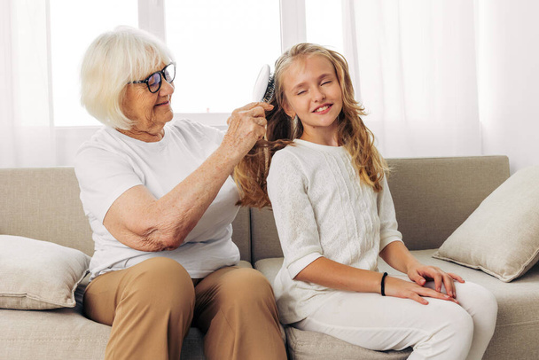 Girl woman love happy grandmother sofa home senior hair old couch comb combing child elderly hair hug mother granddaughter lifestyle family - Photo, Image