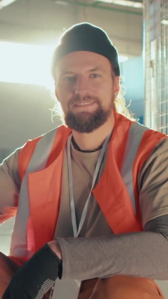 Vertical portrait of smiling Caucasian bearded worker in beanie posing and looking at camera in storehouse - Footage, Video