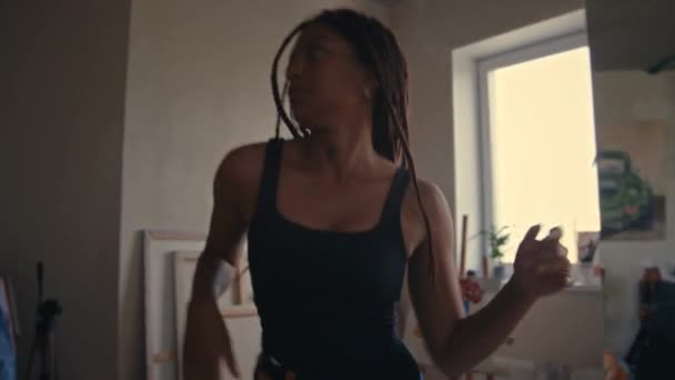Середній нахил привабливої молодої чорної жінки з ковдрами, насолоджуючись танцюючим вільним стилем в сучасній квартирі в стилі лофт з неоновим підписом Хороші вібрації Тільки на стіні - Кадри, відео