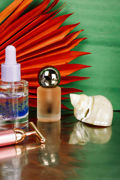 Makeup products and seashell on green background. Beauty products on a stone podium. Serum bottle with essential oil, perfume. Female lifestyle. - Photo, Image