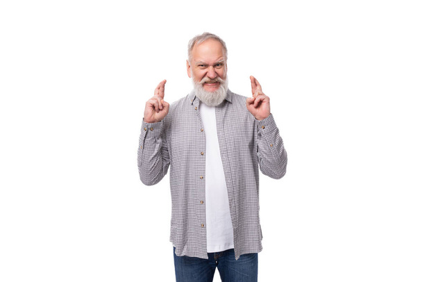 καλοντυμένος ηλικιωμένος με γκρίζα γενειάδα και μουστάκι ντυμένος με καρό πουκάμισο σταυρώνει τα δάχτυλά του.. - Φωτογραφία, εικόνα