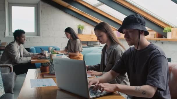 Medium shot of busy Caucasian, African American and Asian male and female customers sitting on couches in flexible use office facility, working with laptops, gadgets and documents - Footage, Video