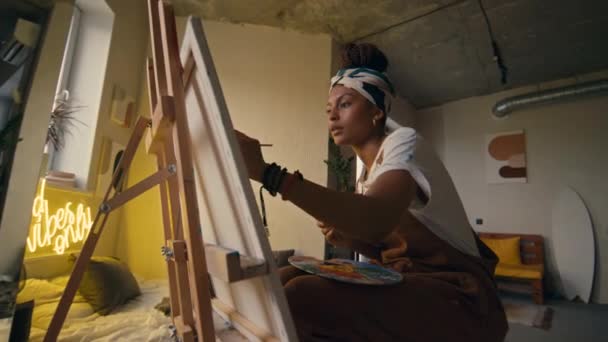 Μέση χαμηλή γωνία πλάνο της νεαρής Αφροαμερικανής γυναίκα-ζωγράφος δημιουργώντας νέα έργα τέχνης χρησιμοποιώντας ζωντανή μπογιά στο διαμέρισμα σοφίτα grunge - Πλάνα, βίντεο
