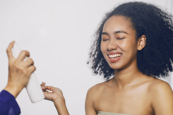 Молодая афро-американская черная женщина ложится, в то время как лицевик использует крем для лица и маску, чтобы питать свою кожу в спа-салоне отеля. - Фото, изображение