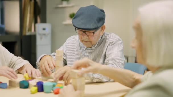 Video s bočním cestováním tří seniorů hrající si s dřevěnými dovednostními deskovými hrami v pečovatelském domě - Záběry, video