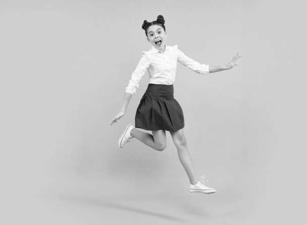 Happy funny jumping teenager. Happy schoolgirl, positive and smiling emotions of teen girl. Full length jump of teenager girl on blue isolated studio wear casual skirt and shirt - Photo, Image