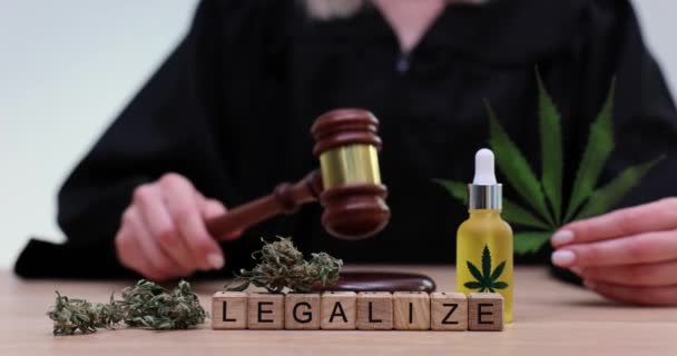 Word legalisatie op houten blokjes op de achtergrond van marihuana en rechter met hamer 4k film slow motion. Juridisch en illegaal cannabisconcept - Video