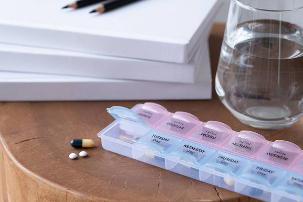 Closeup of medical pill box with doses of tablets for daily take a medicine and glass of water - Photo, Image