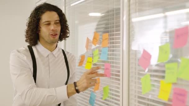 Vídeo en cámara lenta de un hombre señalando un post-it para presentar ideas en una reunión - Metraje, vídeo