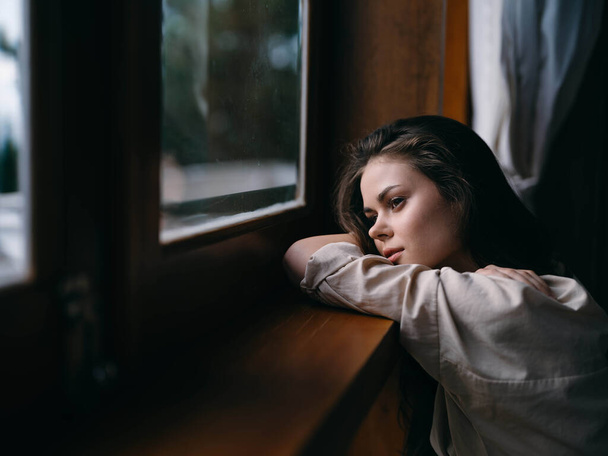 Πορτρέτο της νεαρής γυναίκας στο σπίτι από το παράθυρο με ξύλινο πλαίσιο, φθινοπωρινή διάθεση, άνετο τρόπο ζωής, νυσταγμένος καιρός. Υψηλής ποιότητας φωτογραφία - Φωτογραφία, εικόνα
