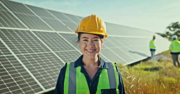 Face of woman at solar panel farm for clean energy, outdoor electricity maintenance and smile. Sustainability, photovoltaic power system and happy technician with helmet for safety inspection - Footage, Video