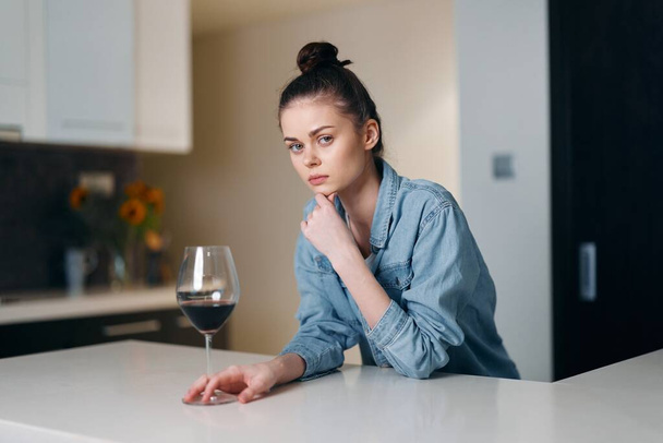 Femme solitaire désespérant dans la solitude, embrasser le verre à vin avec une expression troublée dans l'intérieur de la maison dilatée - Photo, image