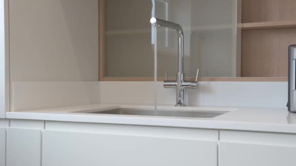 Detailní záběr chromového kuchyňského kohoutku v moderní bílé kuchyni, z níž teče voda. Vysoce kvalitní 4K záběry - Záběry, video