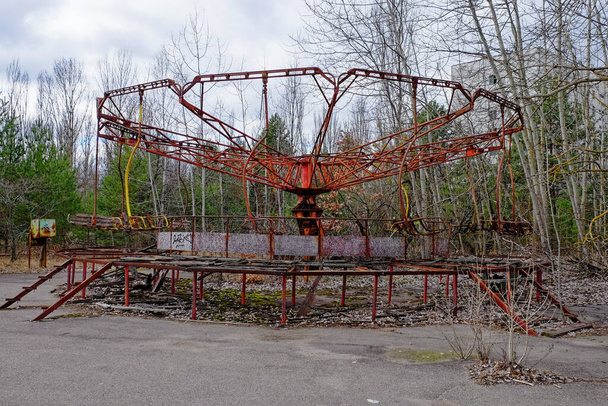 A weathered carousel sits idle, its red paint faded and chipped, surrounded by leafless trees. - Photo, Image