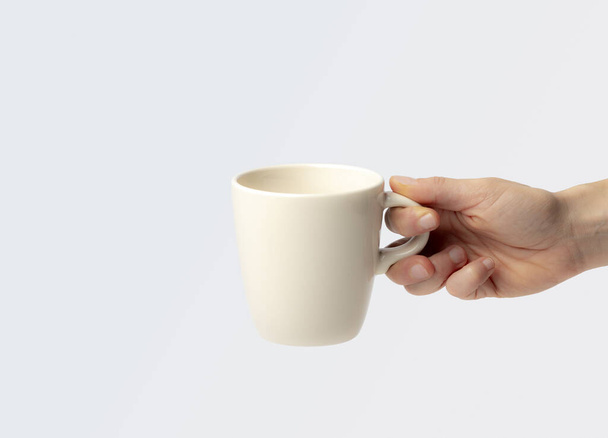 Maquette d'une tasse, tenue par la main d'une jeune femme, comme si elle attendait d'être remplie de café chaud, ou de chocolat, sur un fond uni - Photo, image