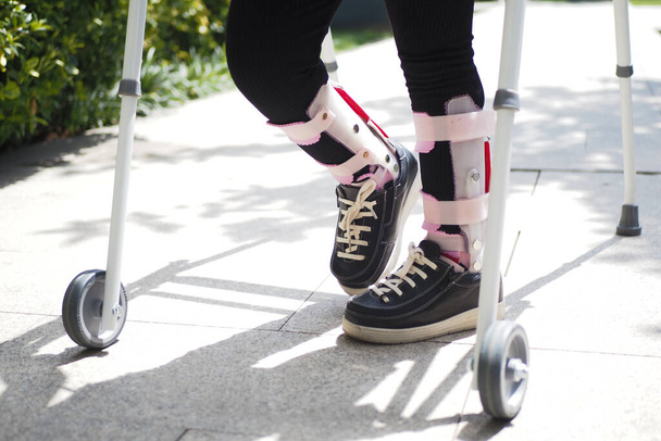  child with walking frame and knee orthosis outdoor . - Photo, Image