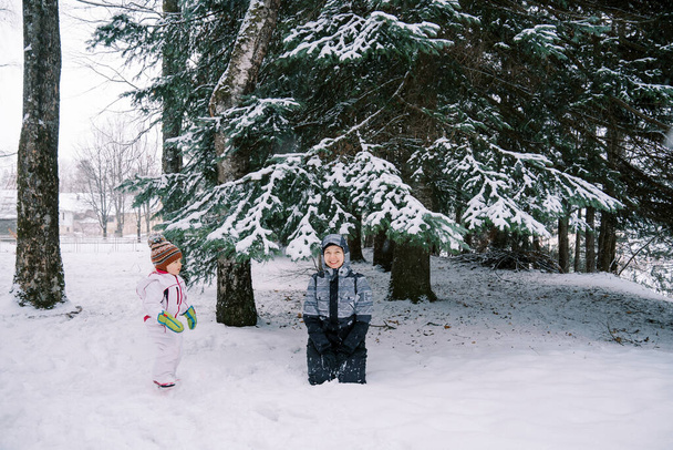 A kislány a mosolygó anyját nézi, amint egy hófödte fenyőfa alatt ül egy tűlevelű erdőben. Kiváló minőségű fénykép - Fotó, kép