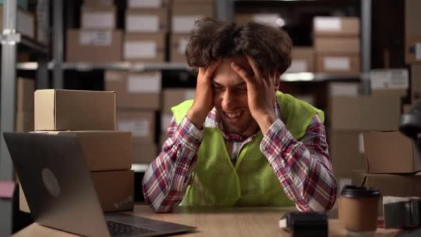 Vermoeide jongeman moe van computerwerk, gestresste man lijdt aan hoofdpijn zitten in het magazijn met behulp van laptop. Kopieerruimte - Video