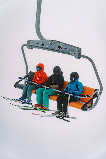 Hiihtäjiä hiihtopuvuissa ja kypärissä ratsastaa tuolihissillä sumuiselle vuorelle. Laadukas kuva - Valokuva, kuva