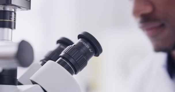 Wetenschap, microscoop en gezicht met de mens in laboratorium voor experiment, vaccin en gezondheidszorg. Analyse, geneeskunde en geneeskunde met Afrikaanse wetenschapper en DNA-onderzoek voor genezing, chemie en studie. - Video