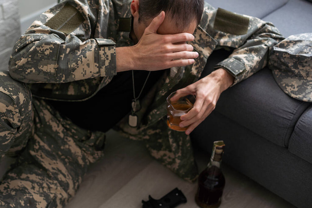 Soldato maschio sconvolto che beve bevanda alcolica in bottiglia a casa e soffre di disturbo post traumatico da stress. Foto di alta qualità - Foto, immagini