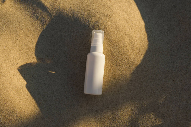 maqueta blanca de un frasco de crema facial o suero con un dispensador sobre arena marina iluminado por la luz del sol. Concepto de cosméticos naturales y orgánicos, productos de belleza - Foto, imagen