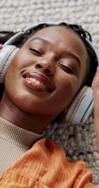 Music, headphones and happy black woman in top view on floor in home, listening to audio or sound to relax. Smile, radio and above of person on carpet streaming song, enjoy technology and eyes closed. - Footage, Video