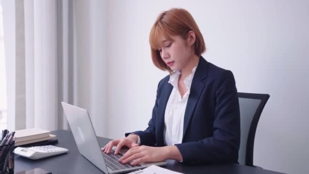 Empresária asiática confiante trabalhando em seu laptop de computador, usando o pensamento analítico para se concentrar em suas tarefas diligentemente. Ela demonstra uma forte ética de trabalho e determinação Imagens de alta qualidade 4k - Filmagem, Vídeo