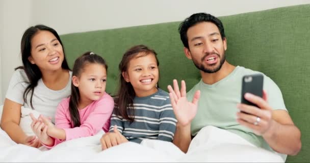 Anya, apa és gyerekek videóhívást az ágyban egy családi otthon a boldogság, a minőségi idő és a kötődés. Egy férfi, nő és lány gyerekek egy hálószobában együtt az online kommunikáció vagy virtuális chat. - Felvétel, videó