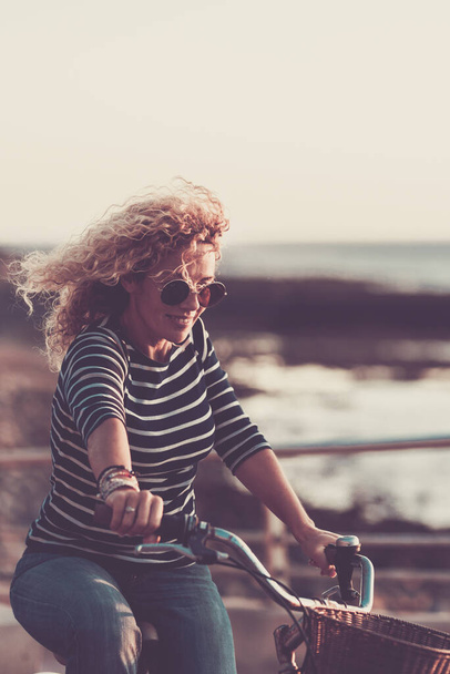  女性は,アウトドアアクティブレジャーアクティビティで自転車に乗って笑顔を楽しんでいます - 白人女性の人々は一人で楽しんでいます - バックグラウンドの海 - 健康的なライフスタイルの概念 - 写真・画像