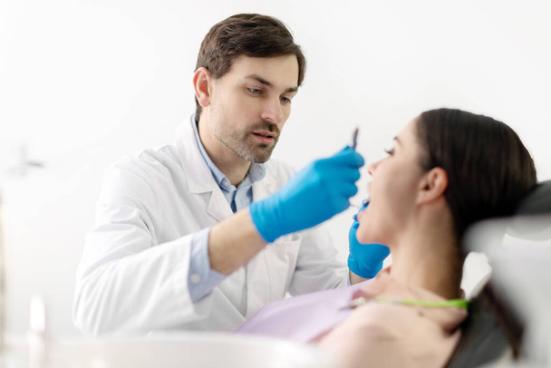 Mężczyzna lekarz stomatolog sprawdzanie zębów młodej damy w klinice, dentysta w rękawiczkach i za pomocą narzędzi - Zdjęcie, obraz