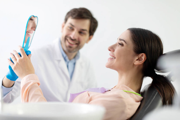 歯科検査中に歯の治療結果を見る鏡を保持する女性患者 気体キャビネットでチェック - 写真・画像