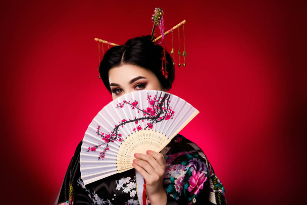 Φωτογραφία του Κορεάτη ντροπαλός χαριτωμένο κυρία κάλυψη πρόσωπο παραδοσιακή γιαπωνέζικη κουλτούρα φεστιβάλ θέμα απομονωμένο σε φόντο κόκκινο χρώμα. - Φωτογραφία, εικόνα