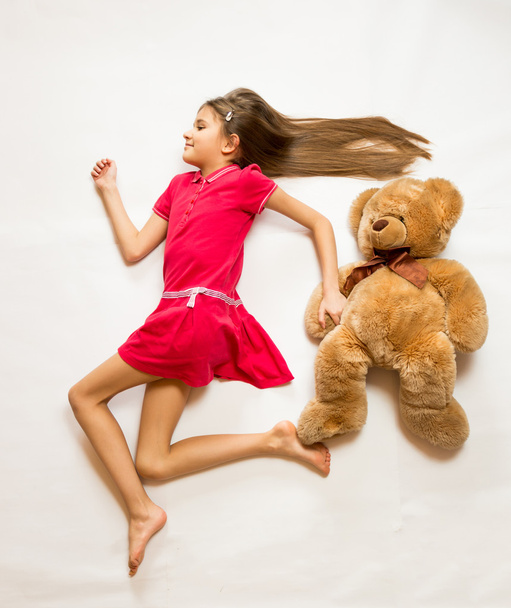  sonriente chica acostada en el suelo y fingiendo correr rápido con Ted
 - Foto, Imagen