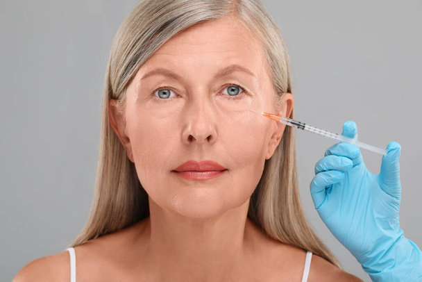 Doctor giving facial injection to senior woman on light grey background, closeup. Cosmetic surgery - Fotoğraf, Görsel