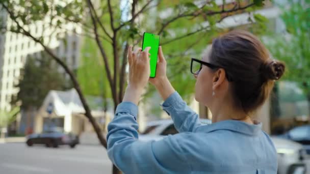 Kadın sokakta dikiliyor ve yeşil ekran, yörünge görüntülü akıllı telefon ile fotoğraf çekiyor. Yavaş çekim. - Video, Çekim