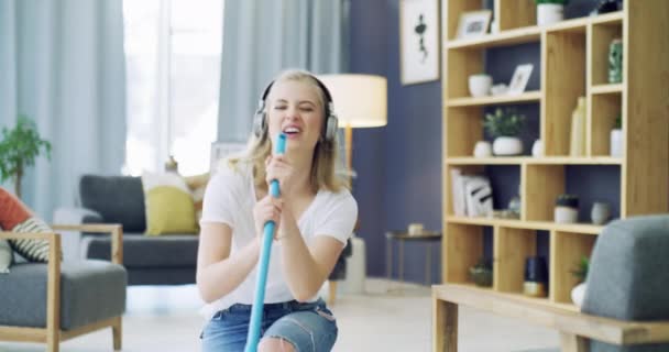 Schoonmaken, zingen en een vrouw met een koptelefoon voor muziek in een huis voor leuke energie en huishoudelijk werk. Jonge vrouwelijke persoon in haar appartement huis met geluk, dansen en vreugde te dweilen en schone vloer. - Video