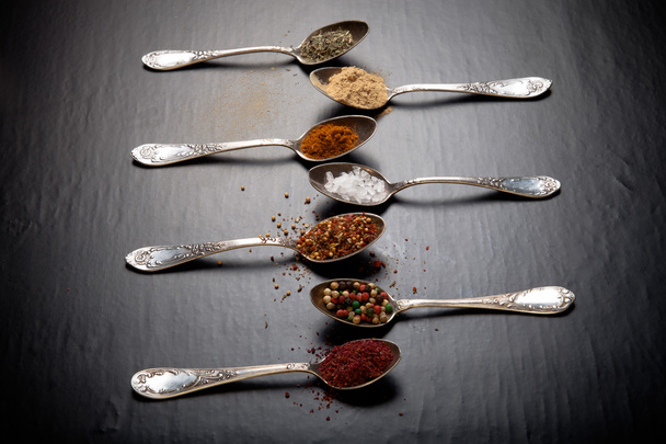 Old metal spoons with different kind of spices on a black backgr - 写真・画像
