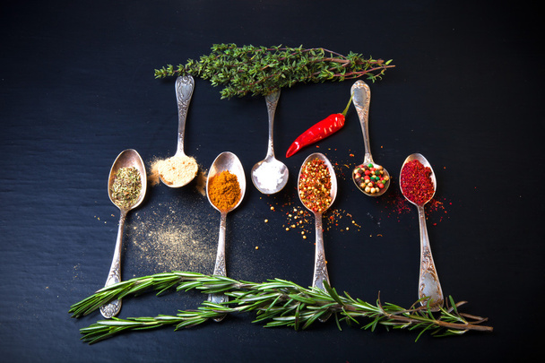 Herbs and spices with old metal spoons on a black background. To - 写真・画像