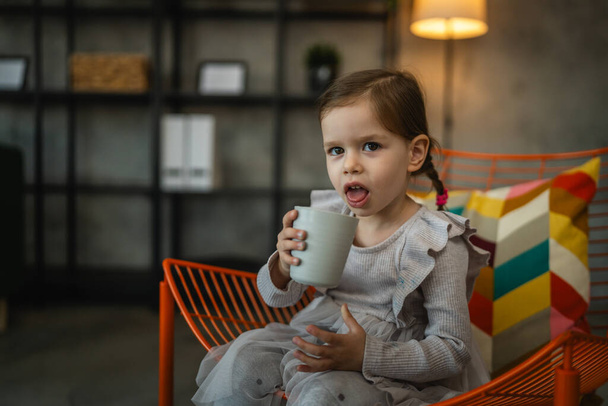 Egy csecsemő lány fehér gyerek gyerek kezében pohár vizet iszik otthon - Fotó, kép