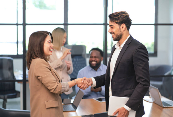 зустріч багаторасового ділового партнерства в офісній кімнаті, азіатська бізнес-леді посміхається тремтячи рукою з кавказьким бізнесменом для майбутнього ділового співробітництва - Фото, зображення