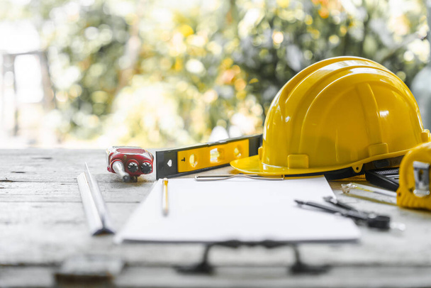 желтый защитный шлем и свернутые архитектурные чертежи на деревянном столе, что указывает на место работы архитектора, возможно, на строительной площадке. - Фото, изображение