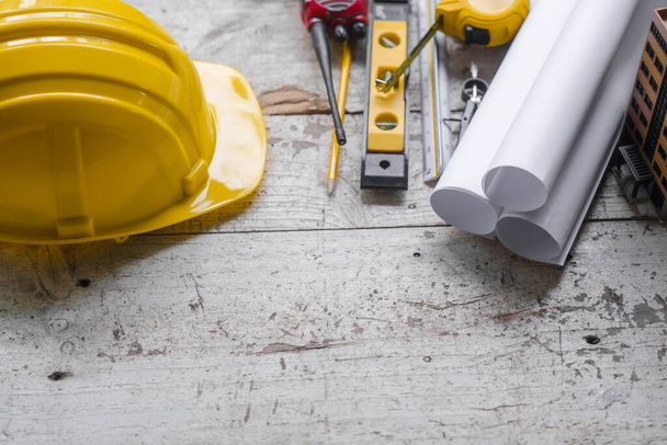 Top view construction tools such as a yellow hard hat, spirit level, measuring tape, folding ruler arrayed against a wooden plank background. - Photo, Image